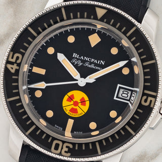 Macro close-up shot of the black dial, yellow No Radiations emblem, and vintage-style lumed markers on a Blancpain Fifty Fathoms