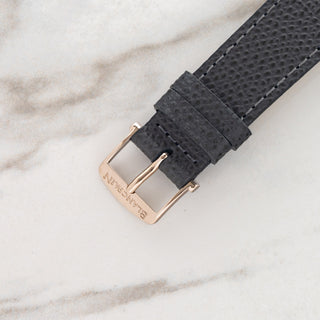 Close-up view of the original signed 18k white gold pin buckle on a textured grey leather strap