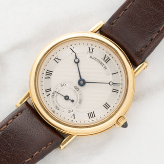 Angled shot highlighting the unpolished 18k yellow gold case, straight lugs, and hand-turned guilloche dial of a Breguet 3210BA