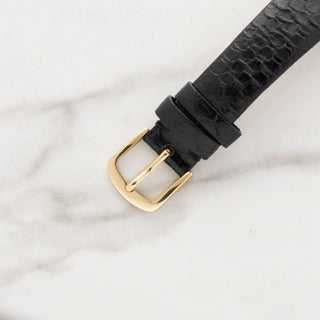 Close-up shot of the gold-toned strap buckle attached to a black leather lizard-grain watch strap.