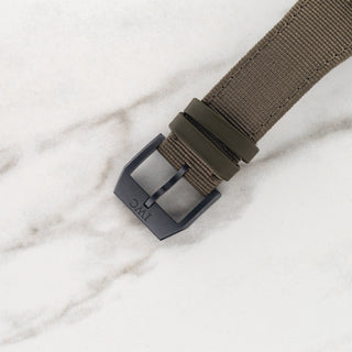 Close-up view of the matte black Ceratanium pin buckle attached to an olive textile strap on an IWC chronograph