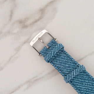 Close-up view of the signed stainless steel pin buckle on a blue denim pattern watch strap