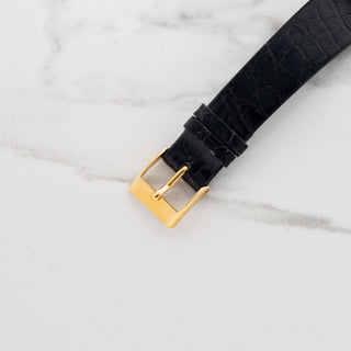 Close-up view of the gold-toned pin buckle attached to a black alligator leather watch strap