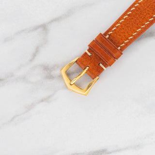 Top view of the signed 18k yellow gold Patek Philippe pin buckle on a textured tan leather strap