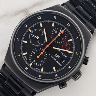 Angled shot highlighting the black PVD coated steel case, 3H red dial logo, and Lemania 5100 chronograph layout on a Porsche Design Orfina 7177