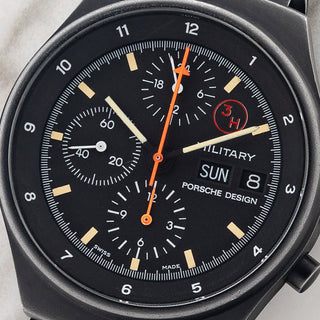 Macro close-up shot of the matte black dial, red 3H tritium emblem, military text, and central orange chronograph hands on an Orfina 7177
