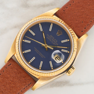 Angled shot highlighting the sharp fluted bezel, unpolished 18k gold case, and matte blue dial of a Rolex Datejust 16018