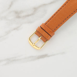 Close-up view of the gold-toned pin buckle attached to a light tan leather watch strap