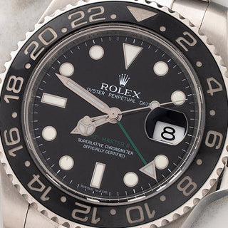 Macro close-up shot of the black dial, green GMT hand, and date aperture with cyclops lens on a Rolex GMT-Master II 116710LN