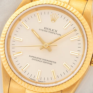 Macro close-up shot of the silver dial, gold stick hour markers, and fluted bezel on an 18k gold Rolex Oyster Perpetual 14238