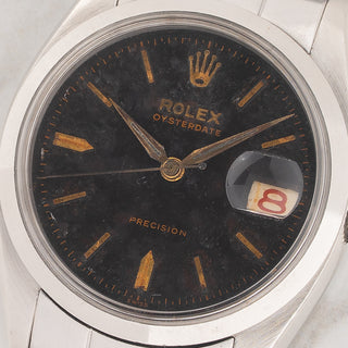 Macro close-up shot of the black gilt dial, gold hands, and red roulette date wheel on a Rolex 6494