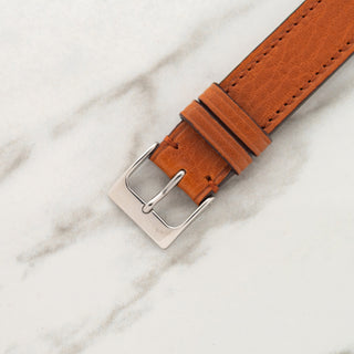 close-up view of the stainless steel pin buckle attached to a textured cognac leather watch strap
