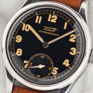 Macro close-up shot of the glossy black gilt dial, warm radium Arabic numerals, and sub-seconds register on a 1940s Tissot Antimagnetique