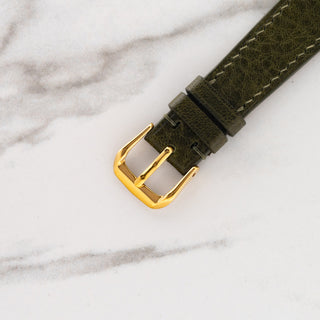 Close-up view of the gold-toned pin buckle attached to a textured olive green leather watch strap