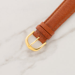 Close-up view of the gold-toned pin buckle attached to a tan pebbled leather watch strap