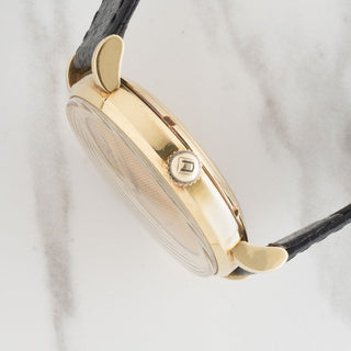 Side profile view showcasing the signed UG acrylic crystal, gold winding crown, and sculpted lug design